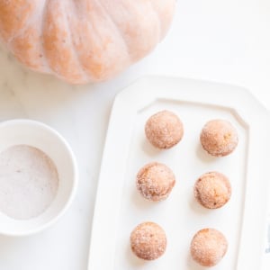 A platter of mini pumpkin muffins with a bowl of sugar and a peach pumpkin in the background.