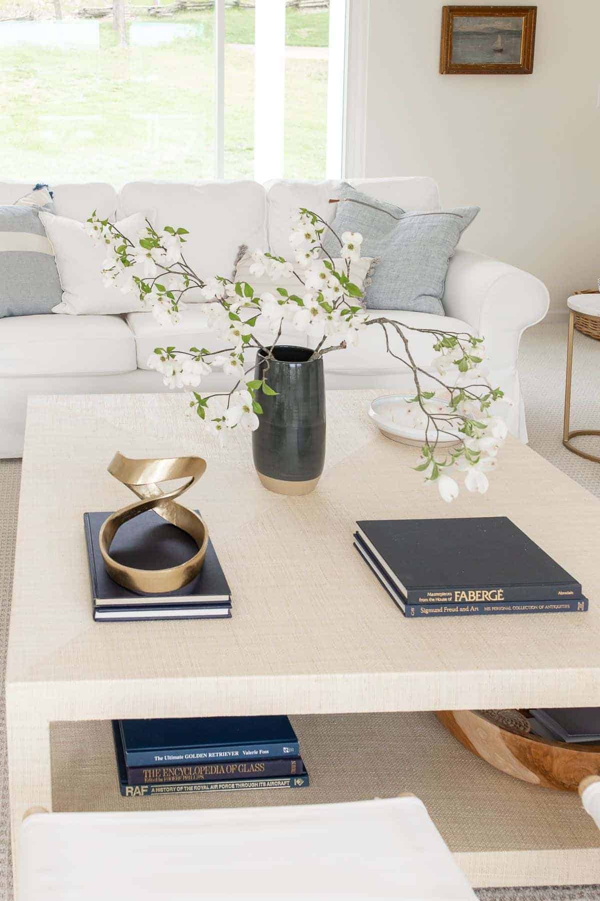 A raffia coffee table decorated in a coastal modern living room style, with a navy vase of blooming branches.