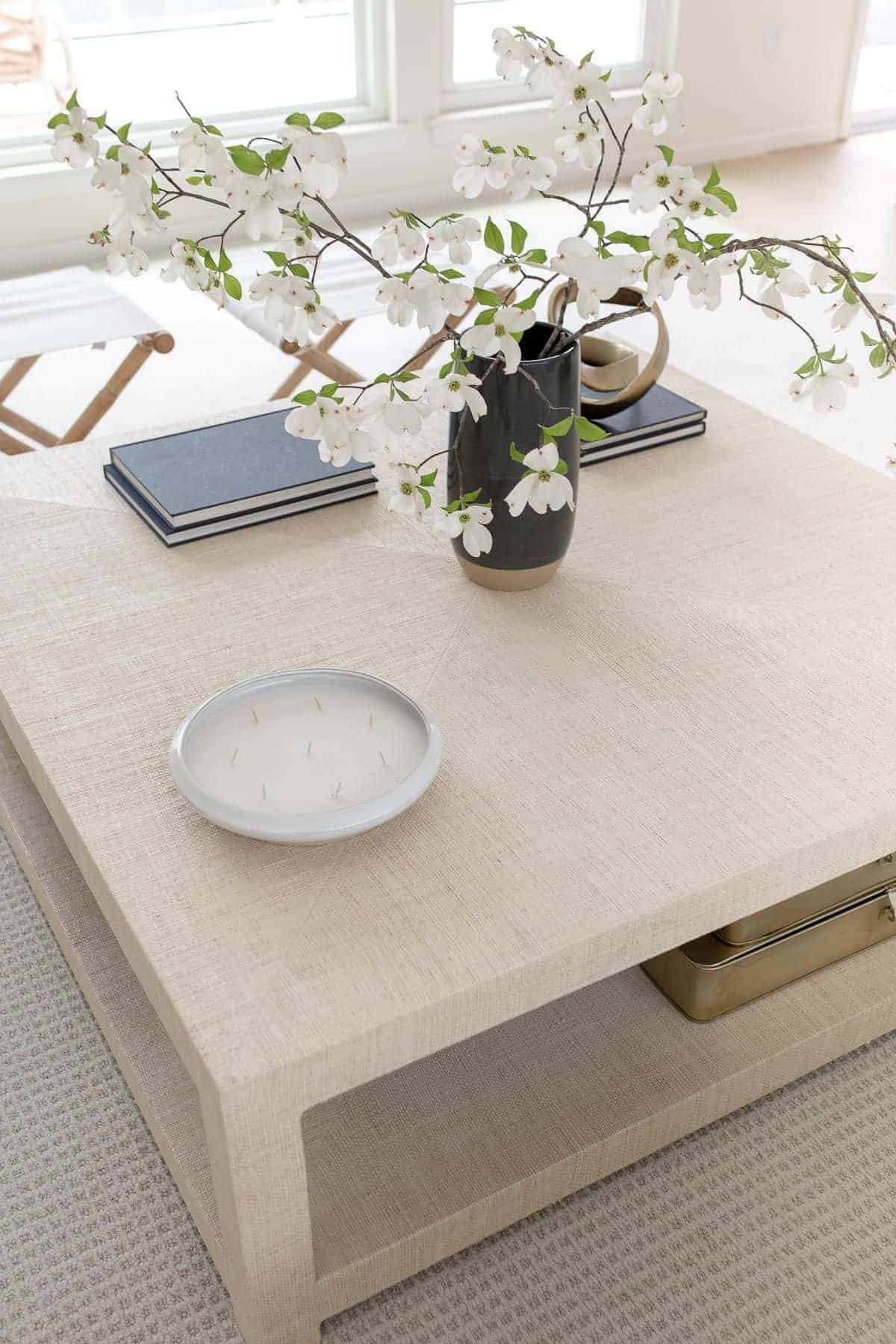 A raffia coffee table decorated in a coastal modern living room style, with a navy vase of blooming branches.