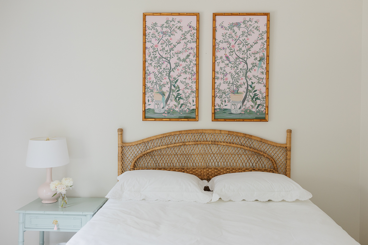 A small bedroom with a wicker headboard and two paintings on the wall.