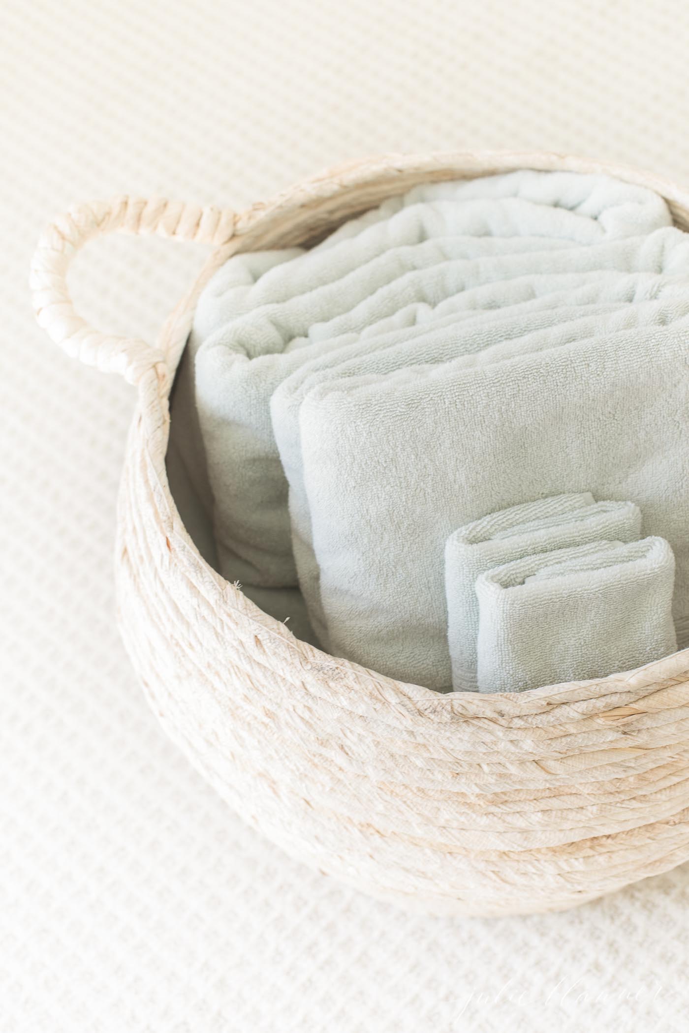 A wicker basket filled with soft green towels in a guest room.