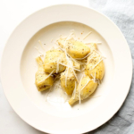 baked artichoke garnished with parmesan in cream serving bowl