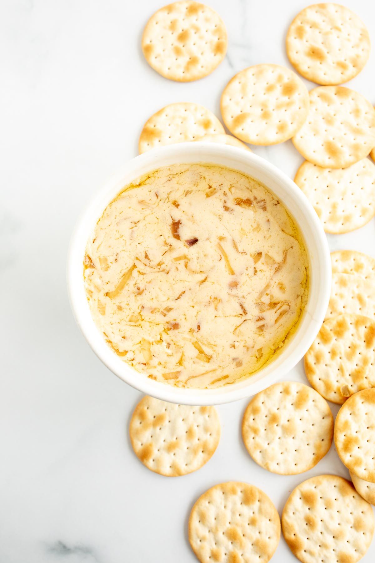 A white bowl of caramelized shallot dip surrounded by crackers