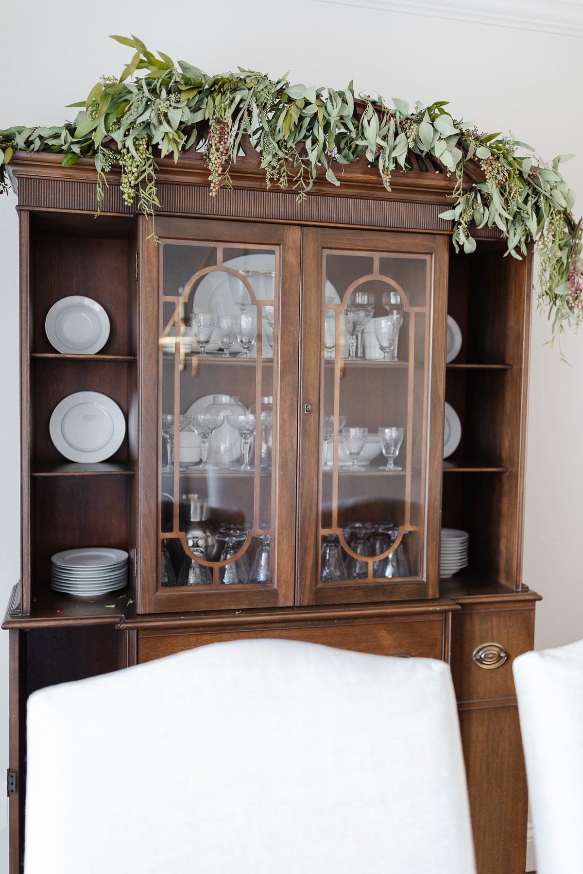 A Christmas house with a dining room adorned with a china cabinet and white chairs.