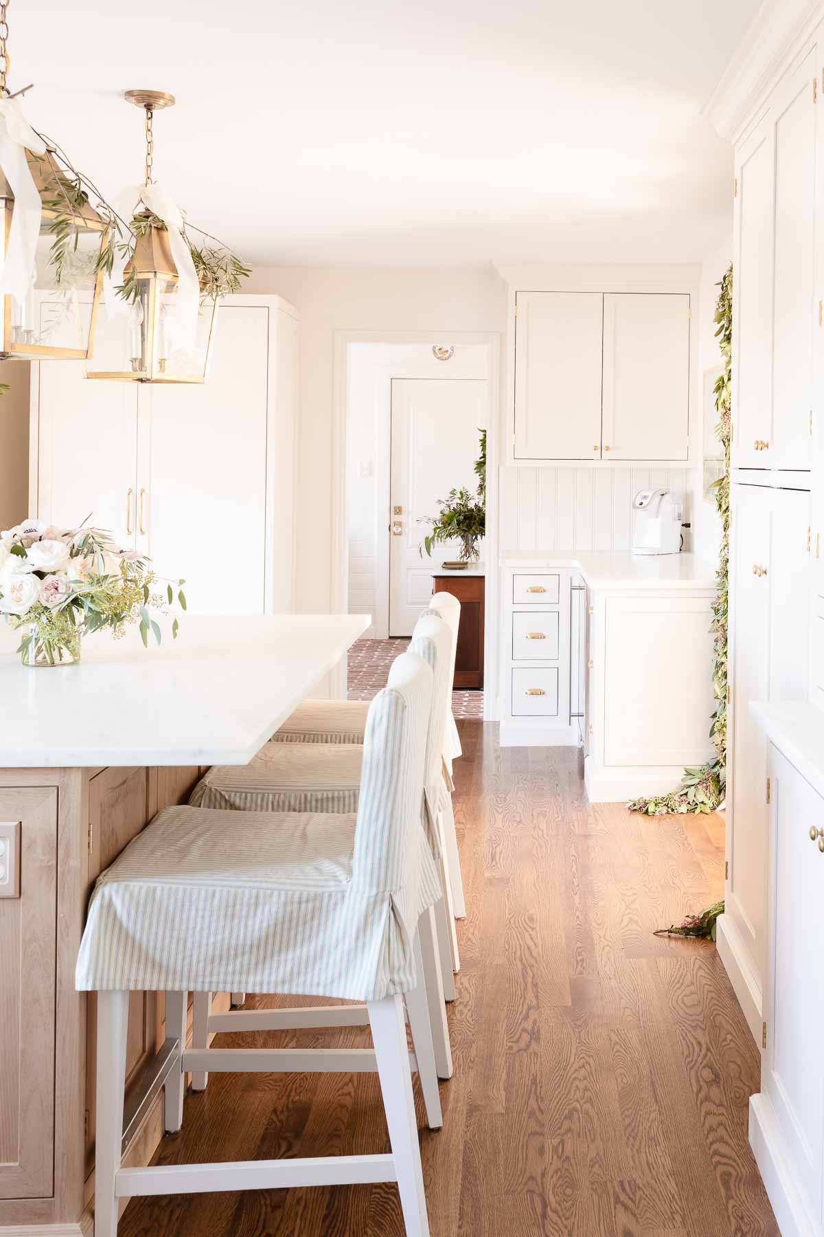 A white kitchen with a white island and chairs, filled with Christmas house decor.