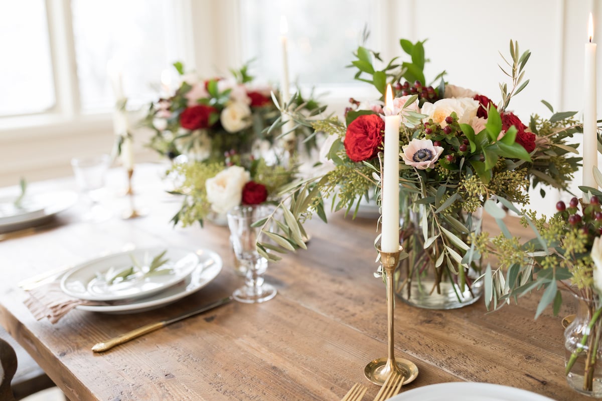 A table setting with flowers and candles on a wooden table in a Christmas-themed house.
