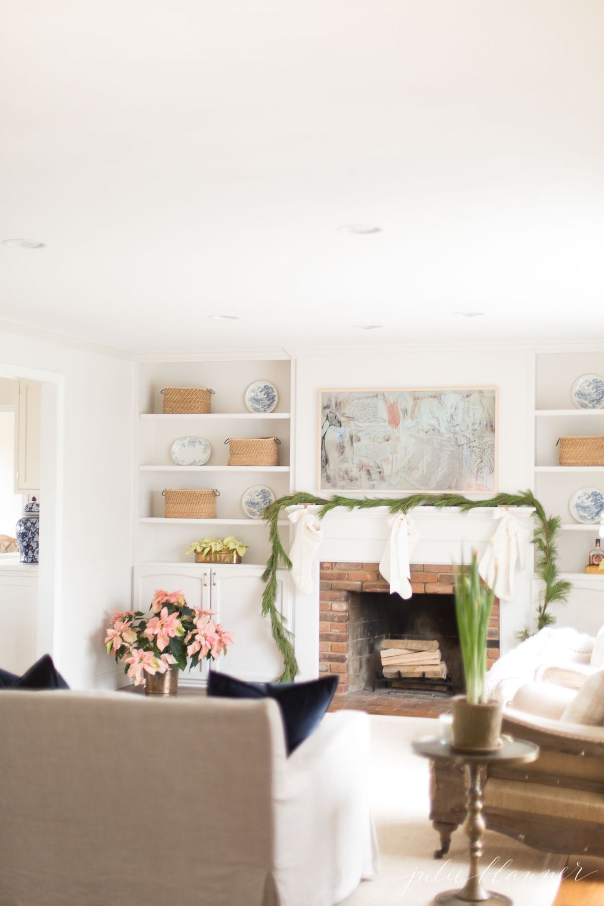A white living room with fresh christmas greenery on the mantel.