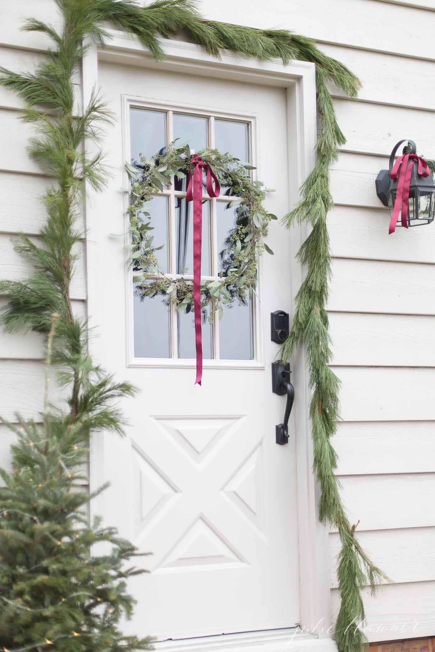 A white door with a window surrounded by fresh pine garland