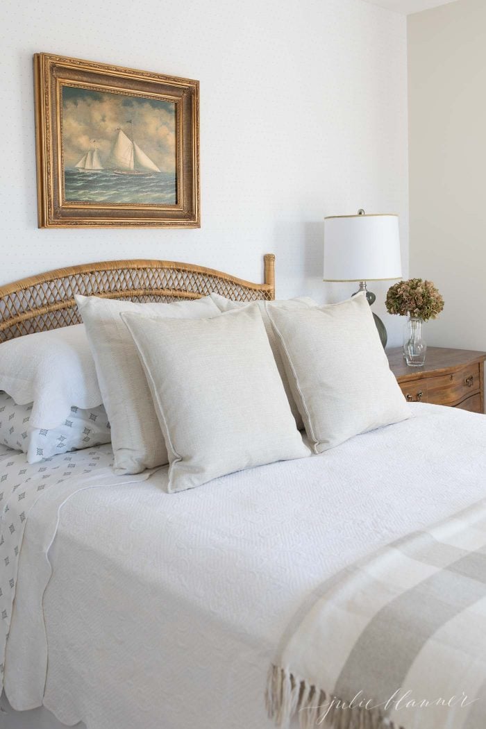rattan headboard with traditional bedding and sailboat painting over the bed
