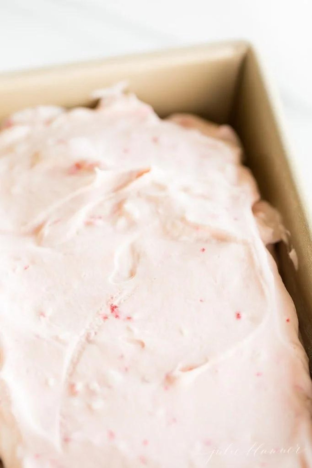 A pink cake with peppermint stick ice cream frosting in a pan.