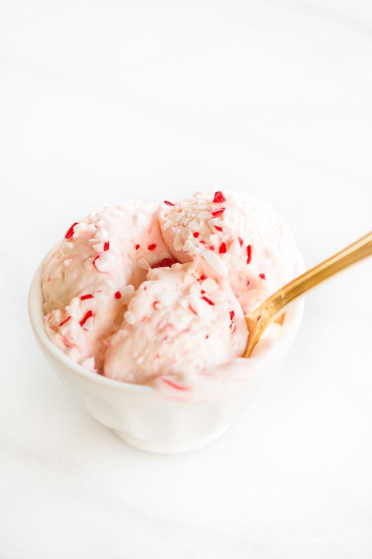Peppermint ice cream in a white bowl with a gold spoon, featuring candy cane ice cream.