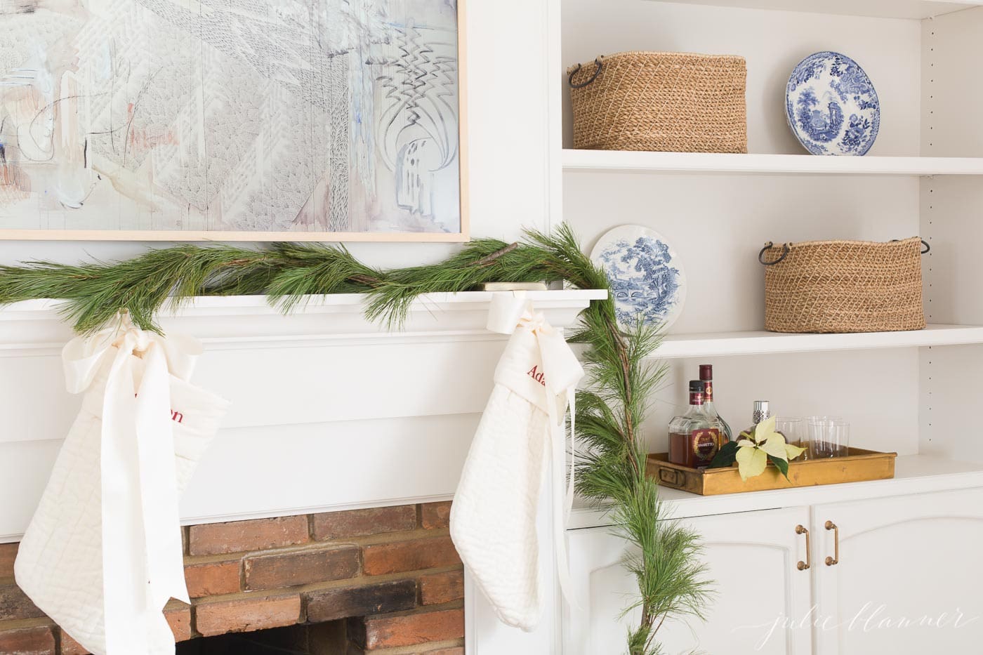 A white living room with a pine garland on the mantel of the fireplace.