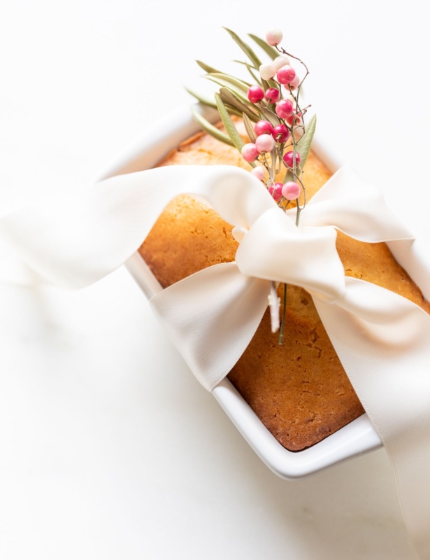 Almond bread in a white loaf pan tied with a white satin bow and a touch of pink berries.
