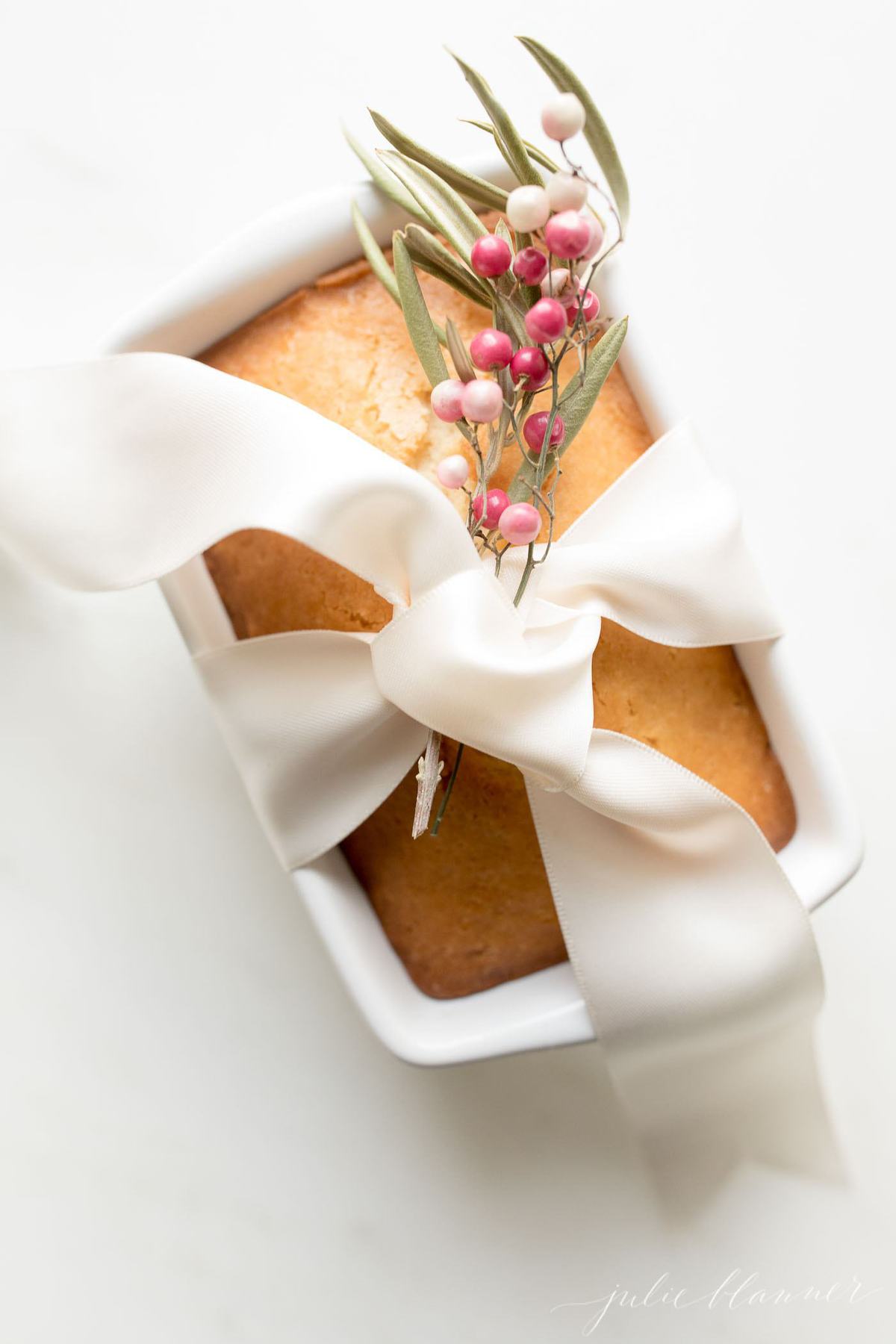 almond bread in white loaf pan with ivory ribbon and garnished with berries for gifting