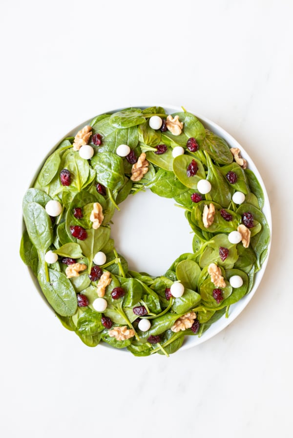 An easy Christmas salad featuring a plate of spinach salad topped with walnuts and cranberries, resembling a festive Christmas wreath.
