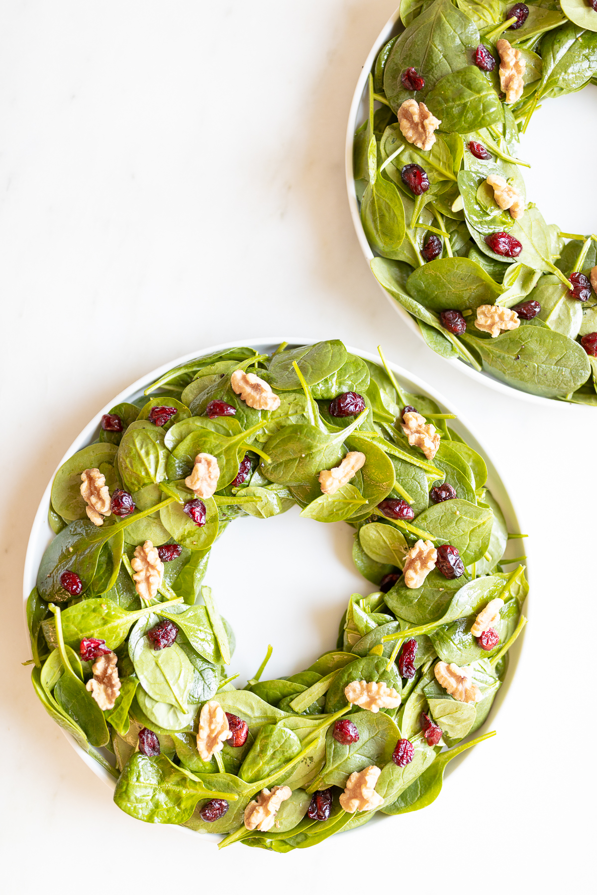 A festive Christmas salad, featuring two plates of spinach and cranberries arranged in the shape of a beautiful wreath.