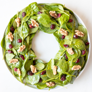 A plate with a Christmas Salad featuring spinach, cranberries and walnuts, beautifully arranged like a festive Christmas wreath.