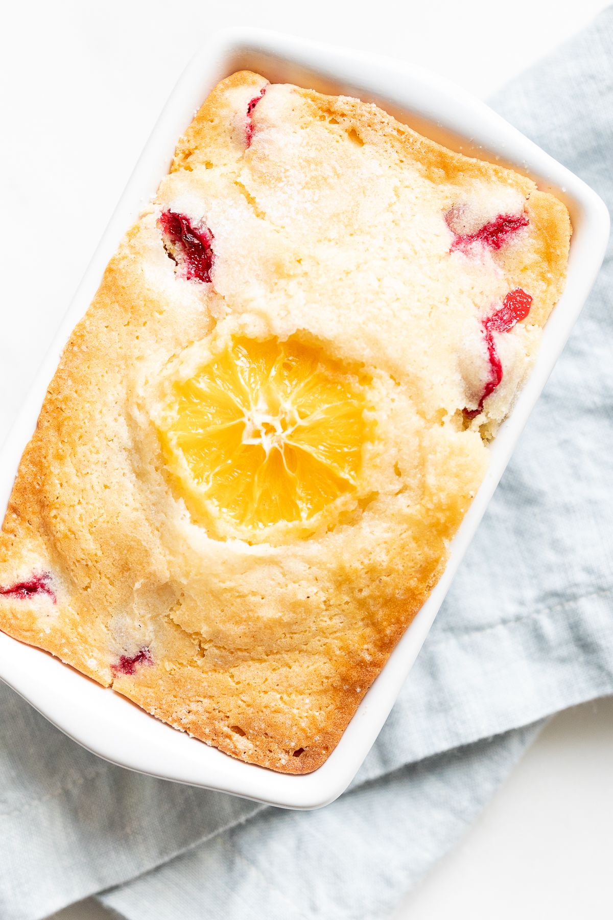 Small ceramic loaf pan of cranberry orange bread, resting on a pale blue linen towel.