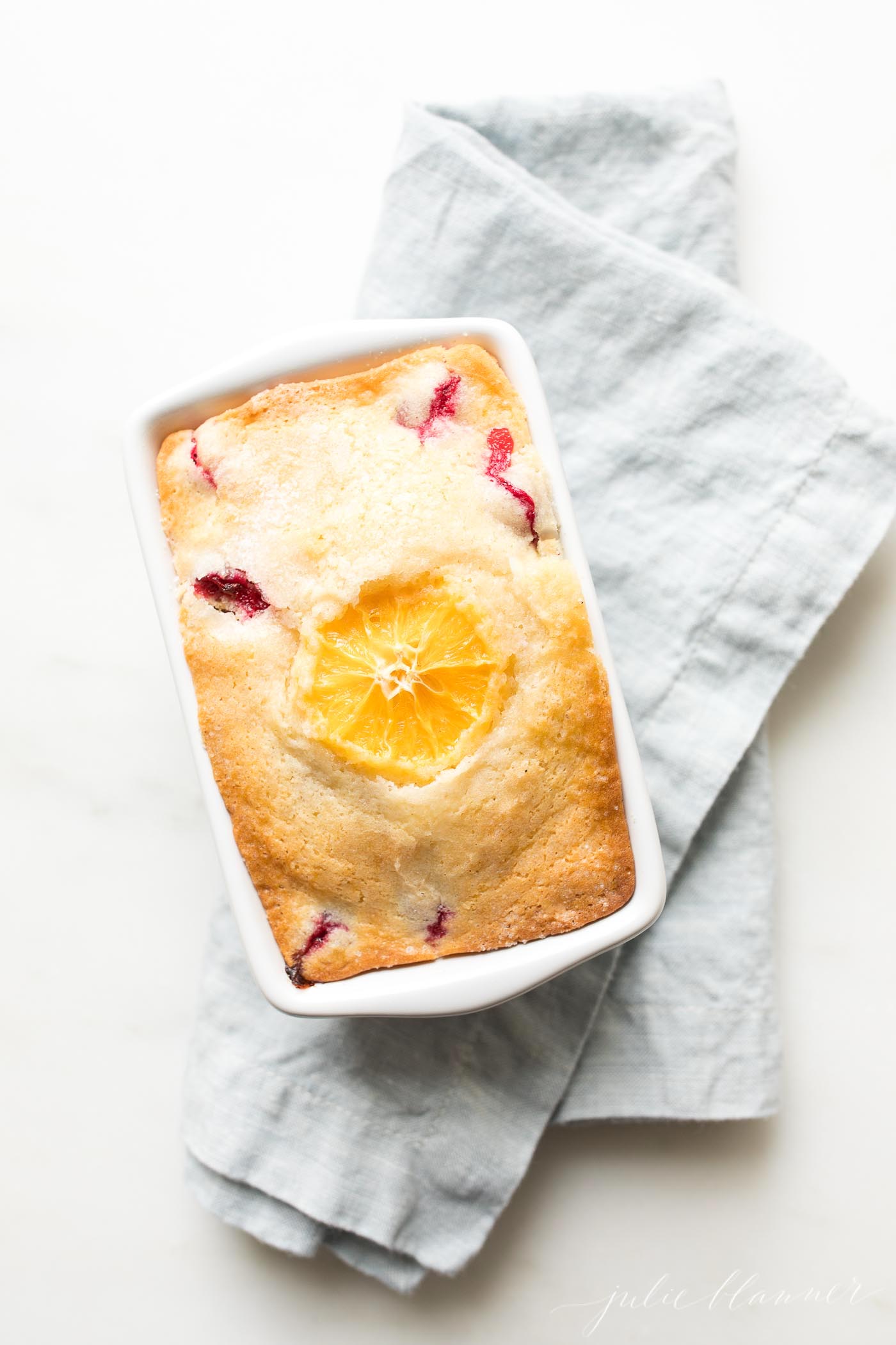 cranberry orange bread in white loaf pan on blue napkin