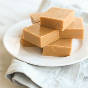 A stack of peanut butter fudge on a white plate, sitting atop a blue linen towel. .