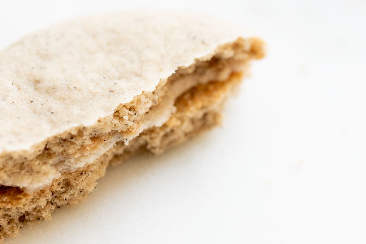 Latte cookie with filling between two layers, broken in half on a white countertop.