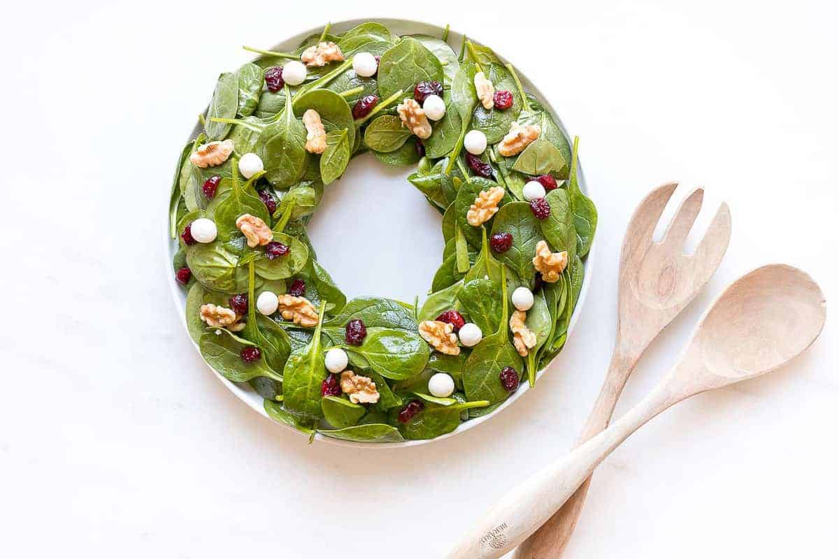 salad in shape of wreath with toppings to look like berries next to wood salad tongs