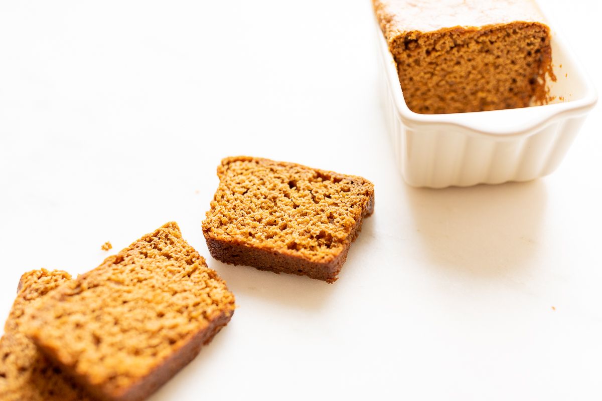 Slices of gingerbread loaf next to a loaf in a white loaf pan.