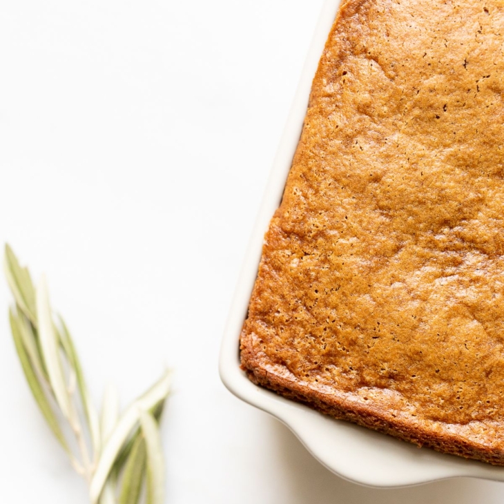 A gingerbread loaf in a white ceramic loaf pan, with an olive branch beside it.