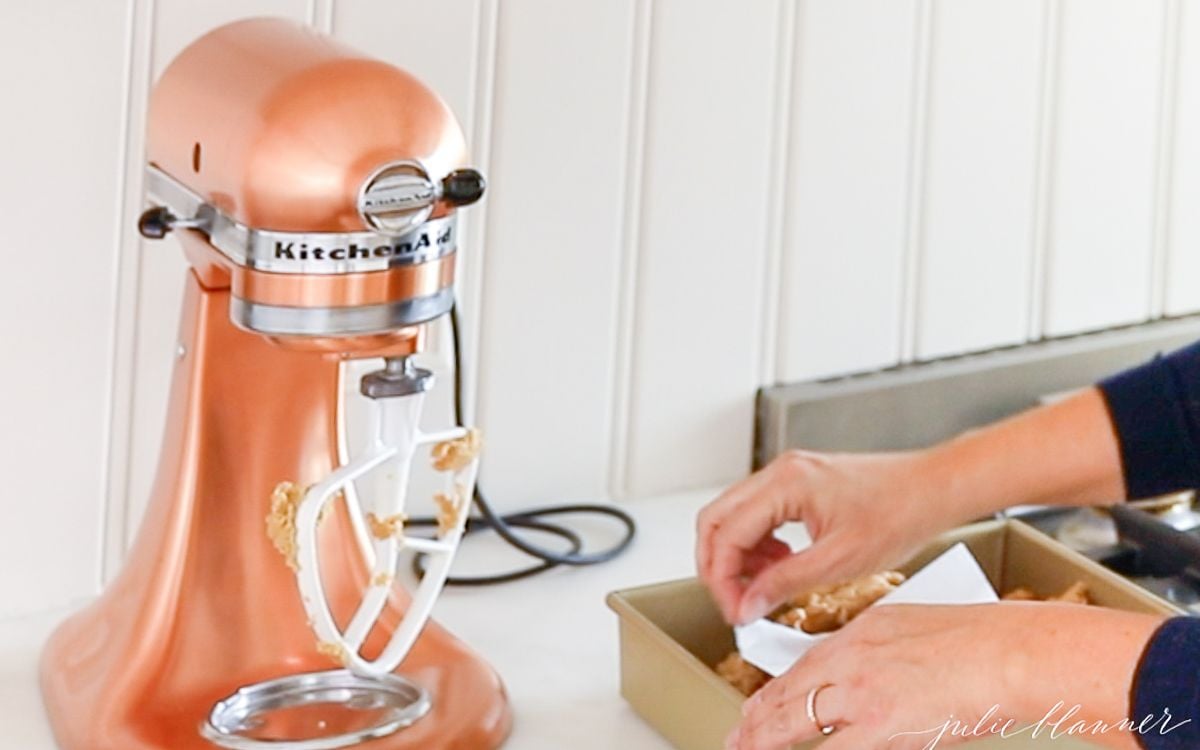 A copper stand mixer with ingredients for peanut butter fudge being added in by a pair of hands.