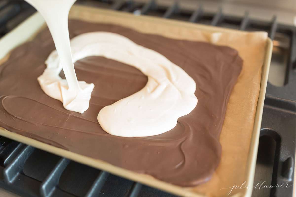 White chocolate Peppermint bark being poured onto a parchment lined baking sheet.