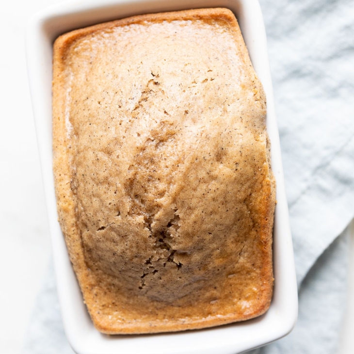 A quick latte bread in a small white loaf pan, on a blue kitchen towel.