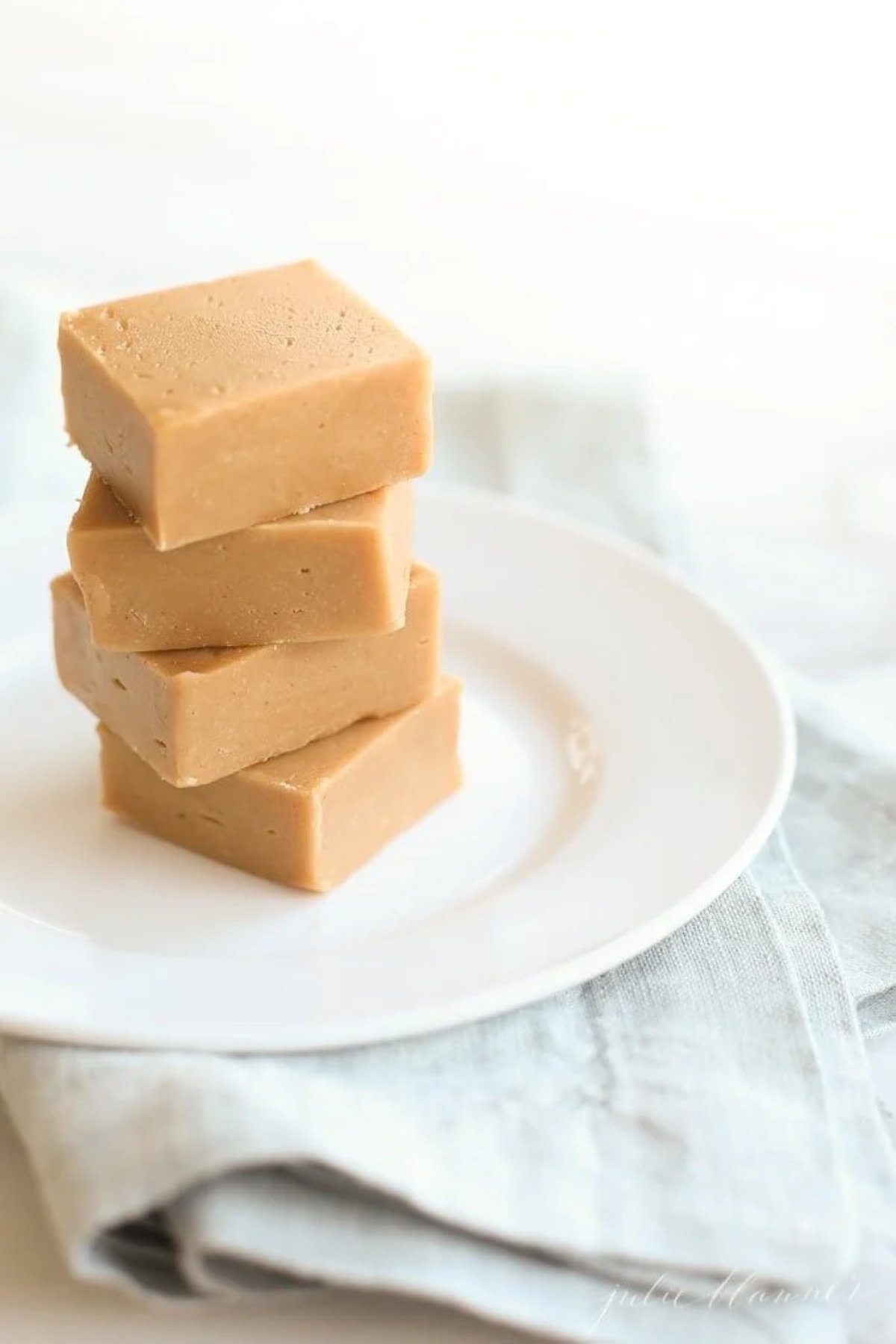 A stack of peanut butter fudge on a white plate, sitting atop a blue linen towel. .