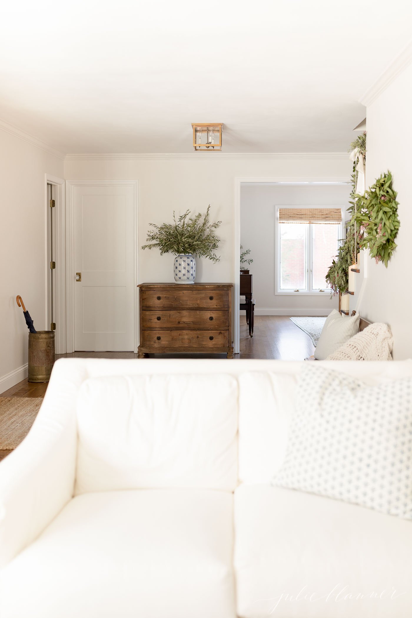 A living room with a white sofa and an open entryway with a chest of drawers beyond.