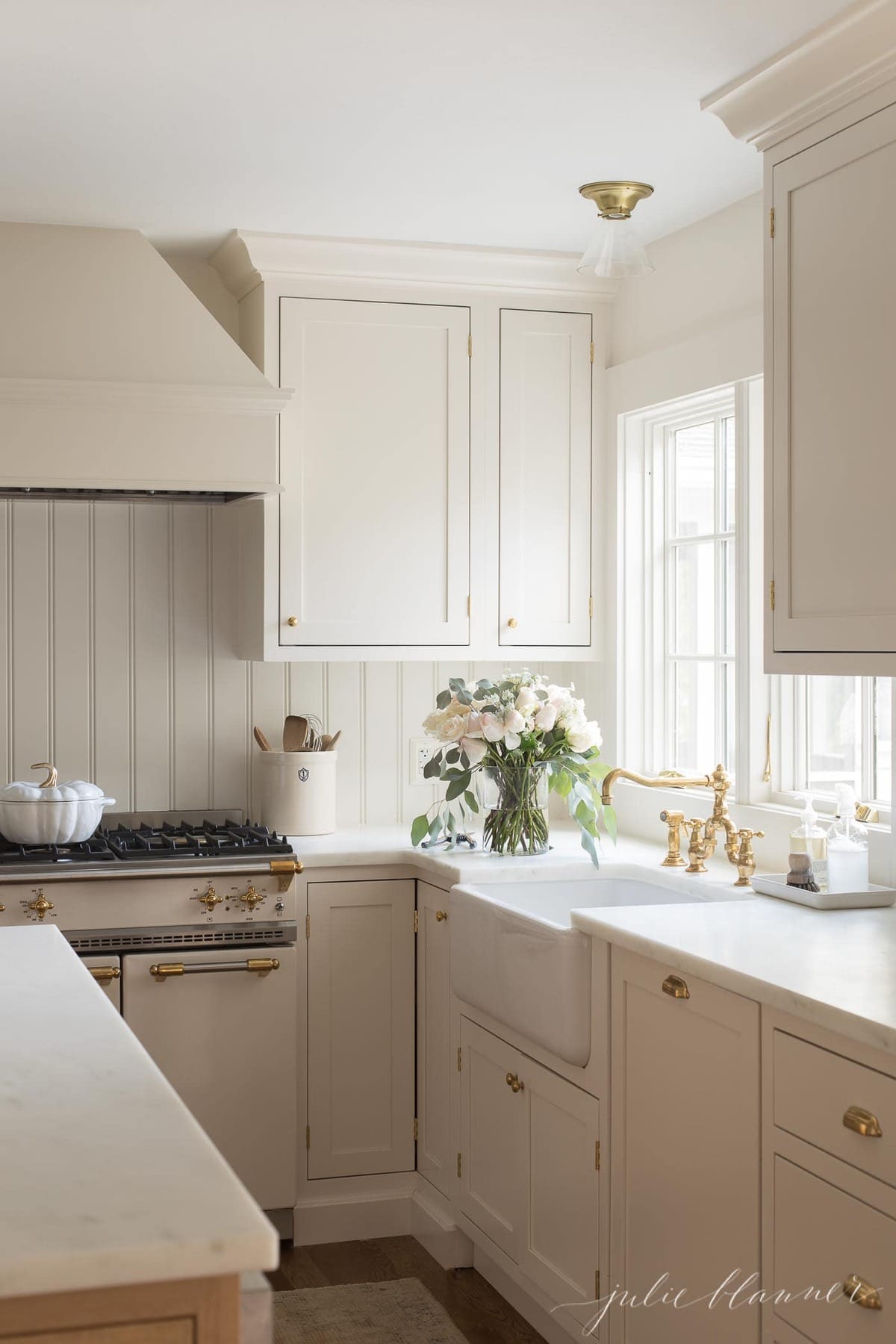 cream cabinets with brass hardware flowers, utensils in a crock and marble counters