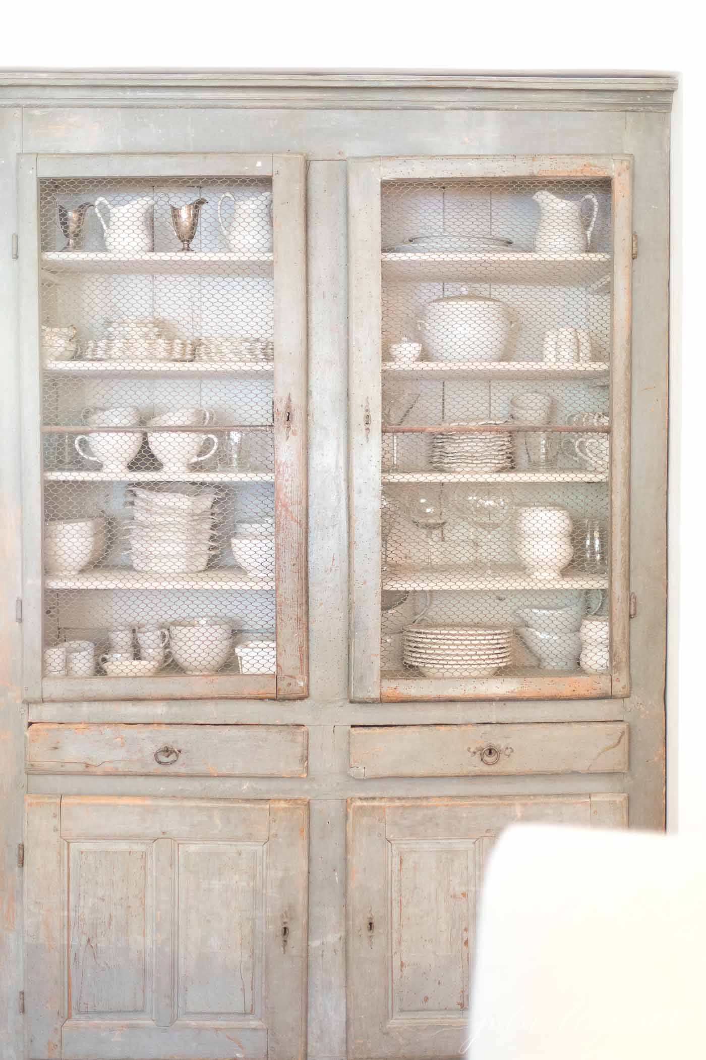 vintage farmhouse cabinet with chicken wire across the doors, white ironstone behind