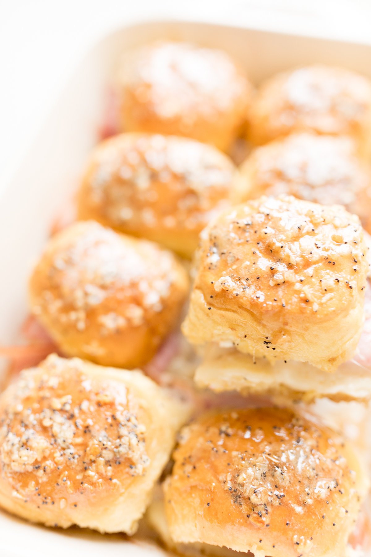 A mouthwatering display of hot ham and cheese sliders, beautifully presented in a white dish.