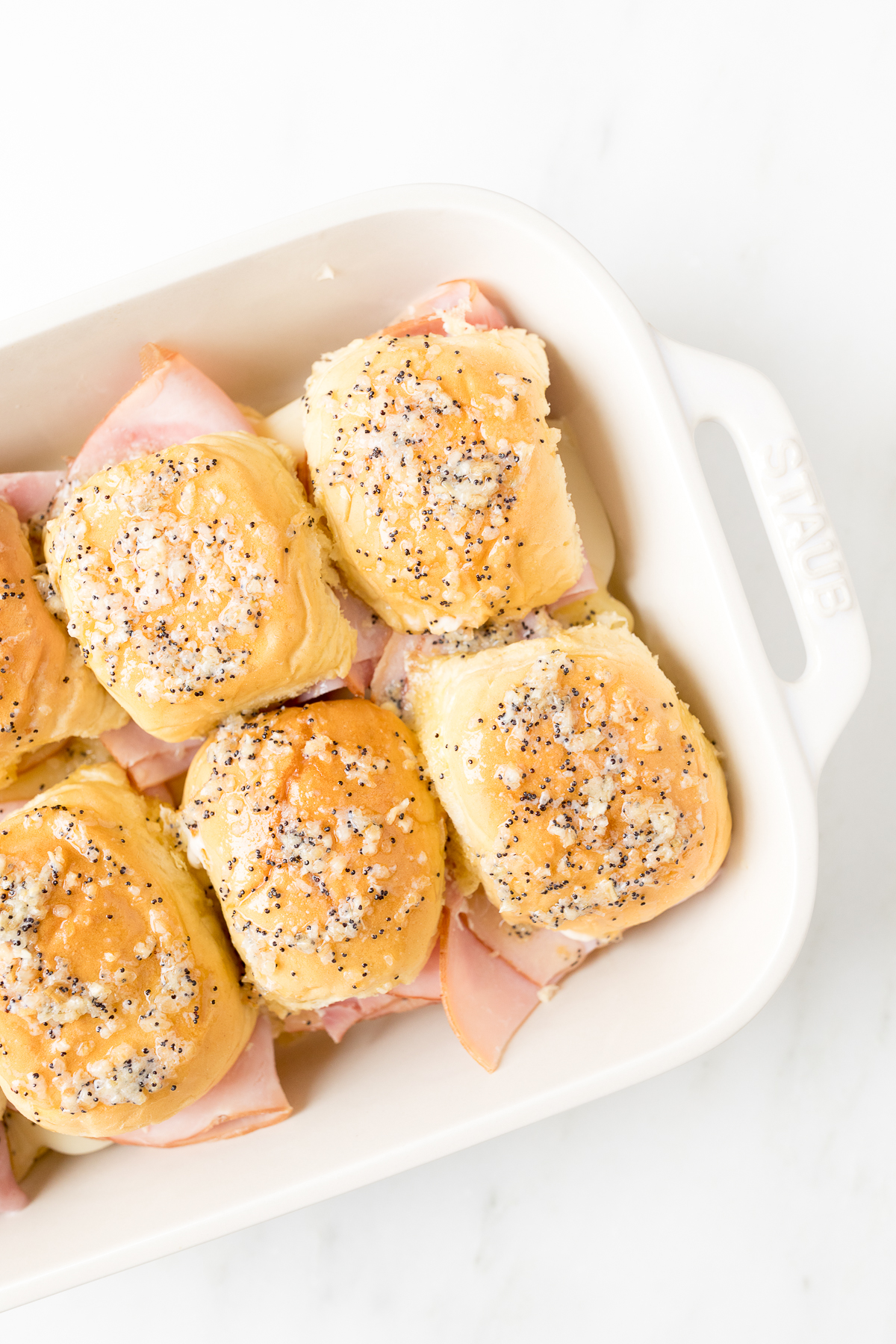 Hot ham and cheese sliders in a white baking dish.