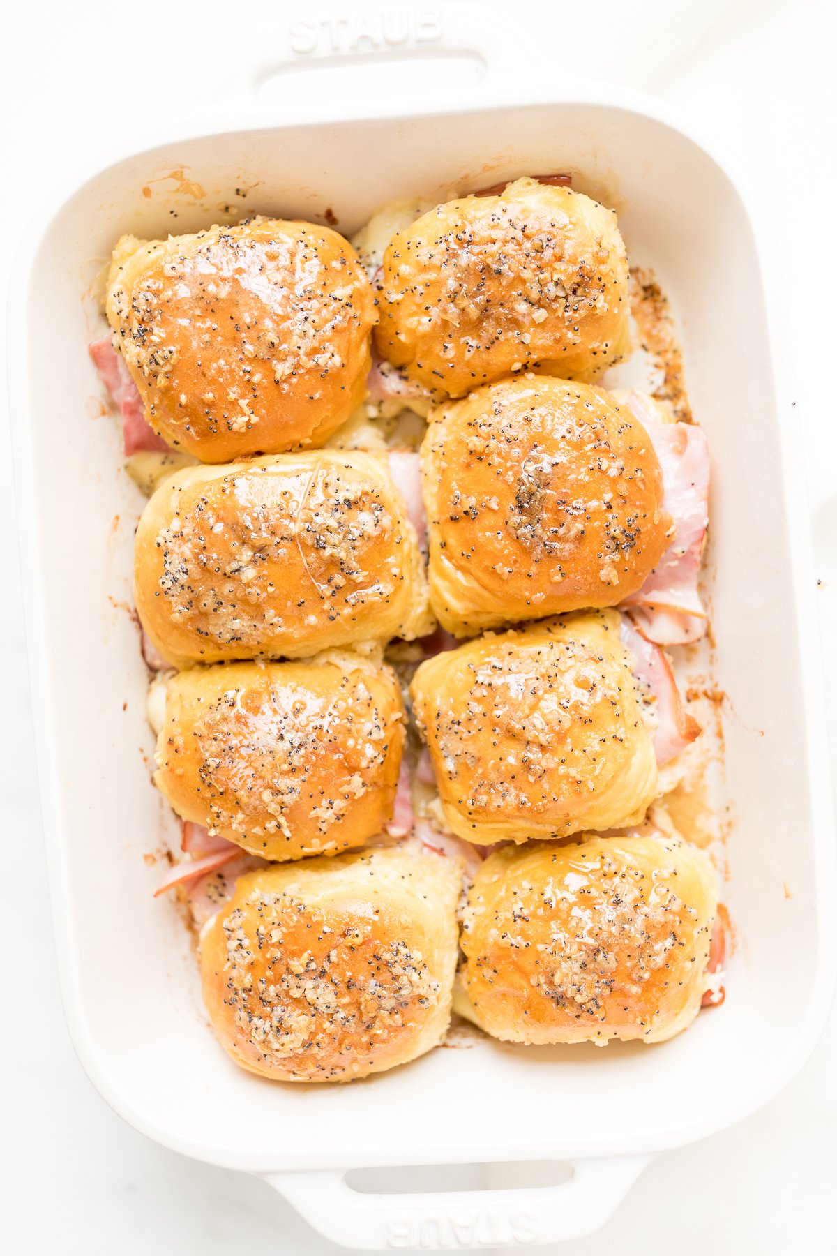 Hot ham and cheese sliders in a white baking dish.