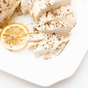Sliced, grilled chicken breast seasoned with herbs and served with lemon sauce on a white plate.