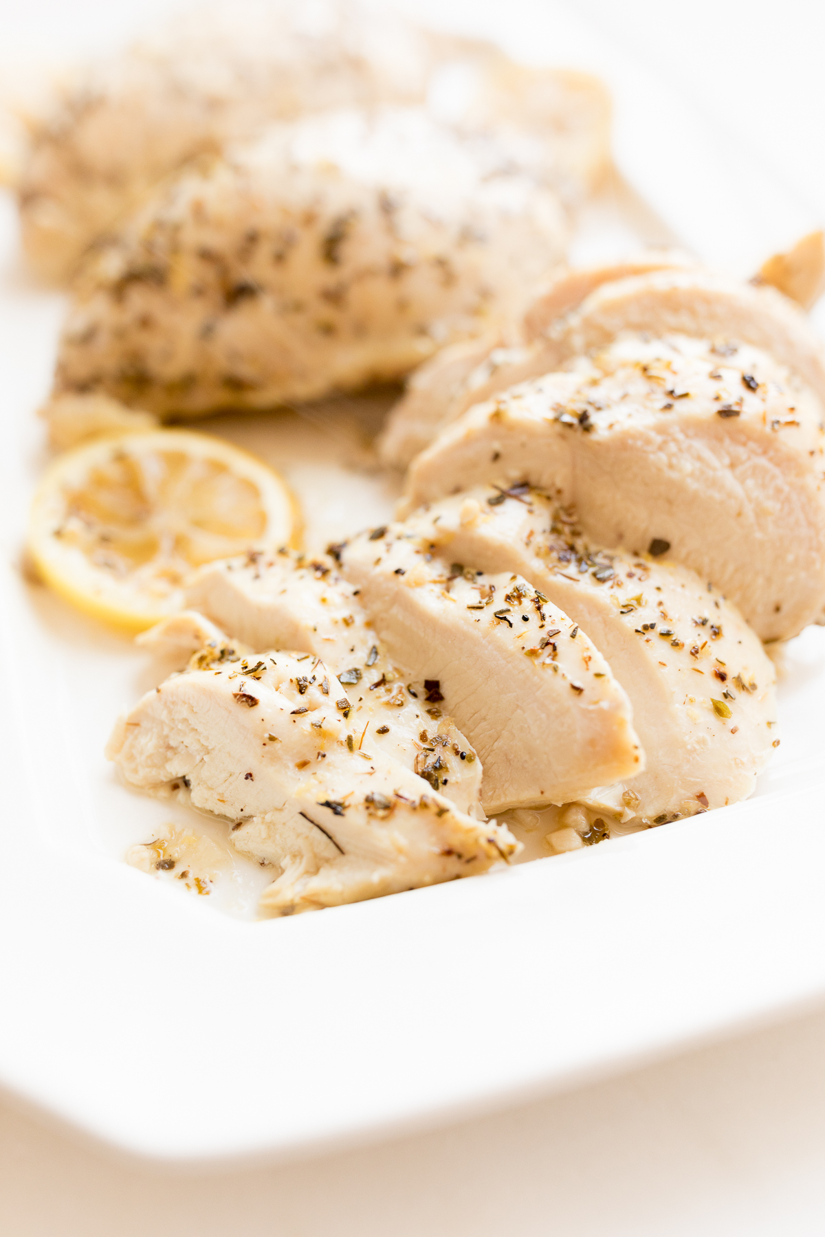 Sliced, herbed chicken breast served with lemon sauce on a white plate.