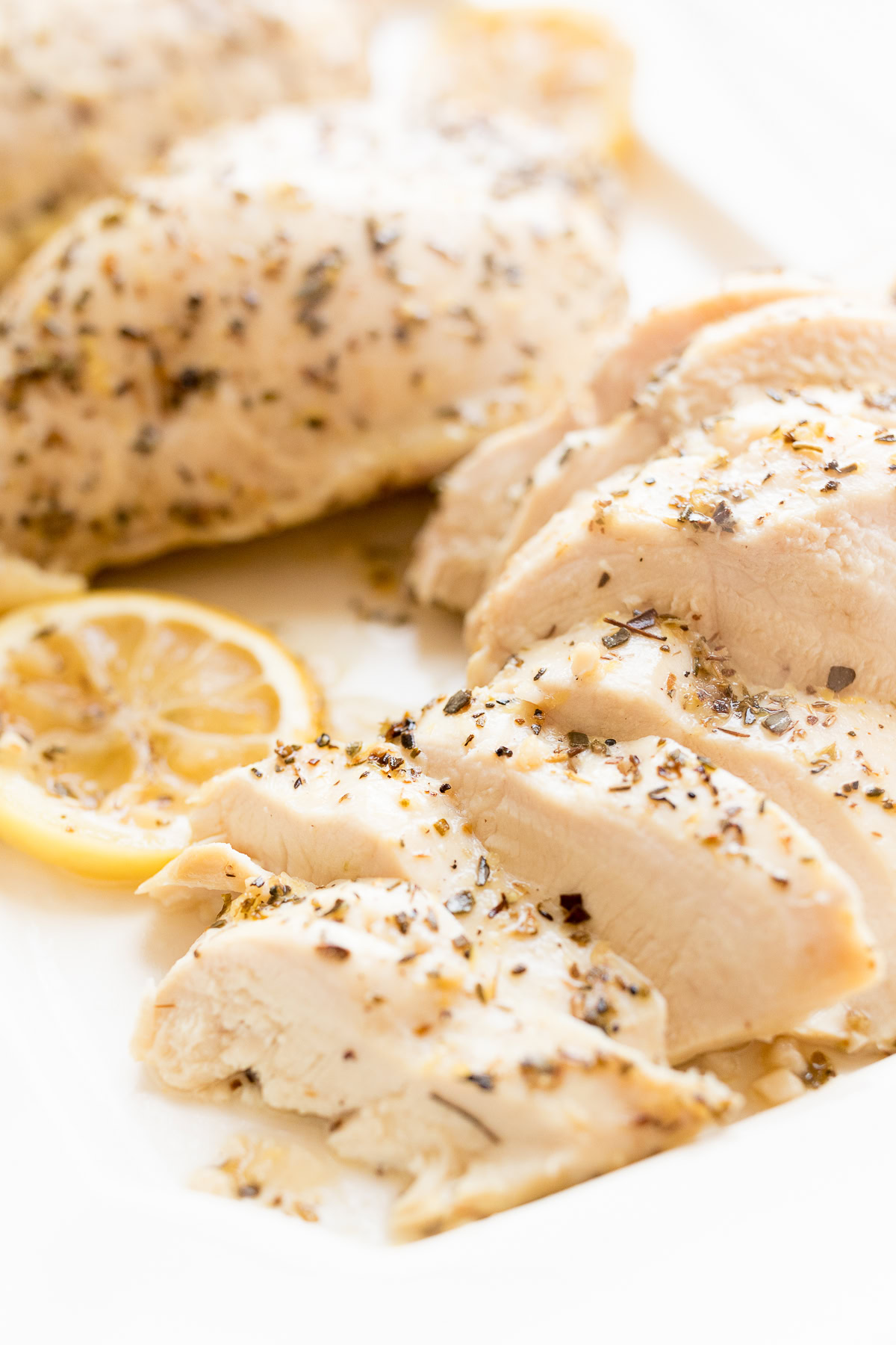 Sliced, seasoned chicken breast served on a white plate with lemon sauce.