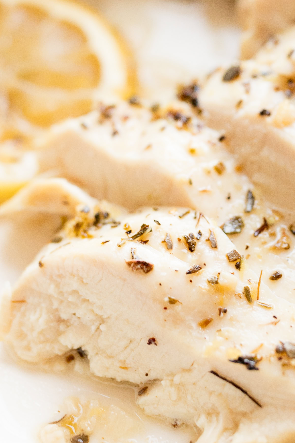 Close-up of sliced, seasoned lemon chicken breast with visible herbs and spices, emphasizing the texture and juiciness of the meat.