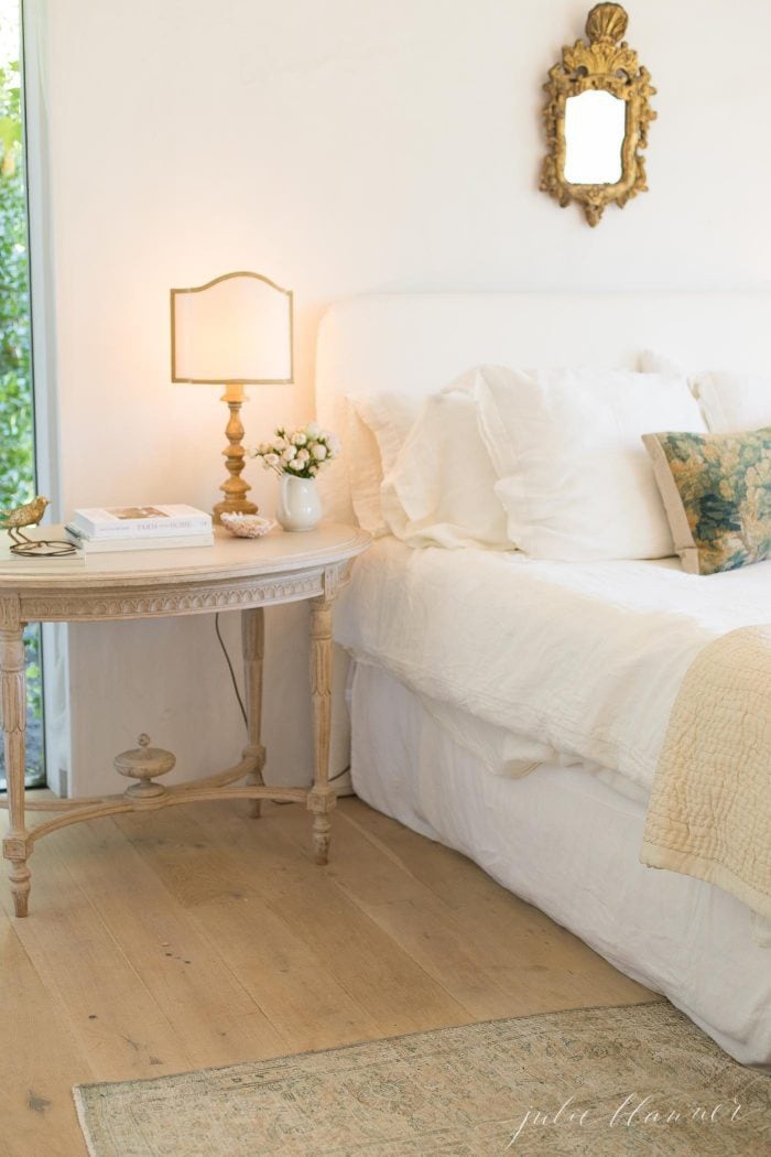 A vintage inspired bedroom with a gold lamp and mirror over the bed