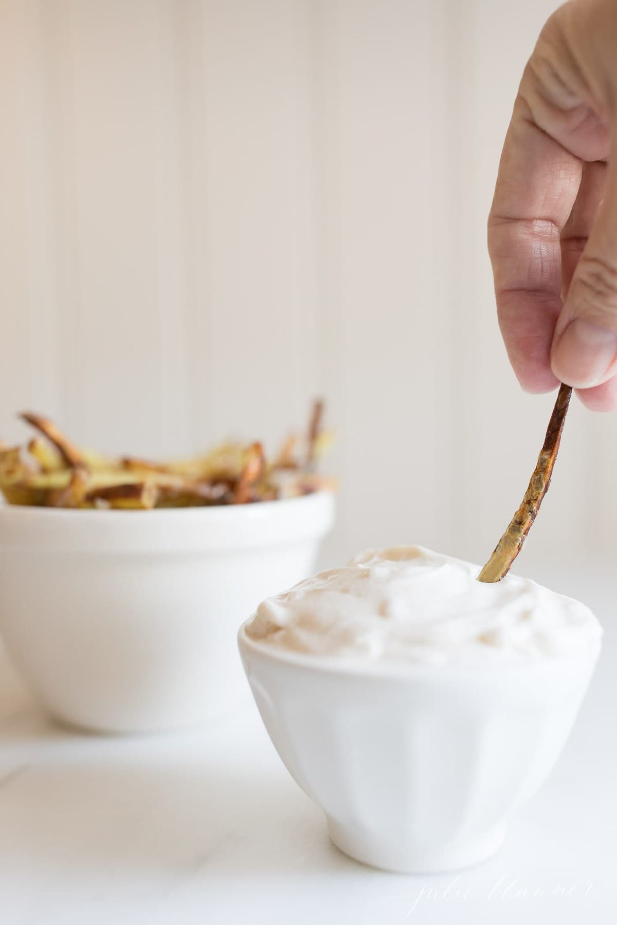 truffle aioli in a white bowl, hand dipping a french fry into bowl