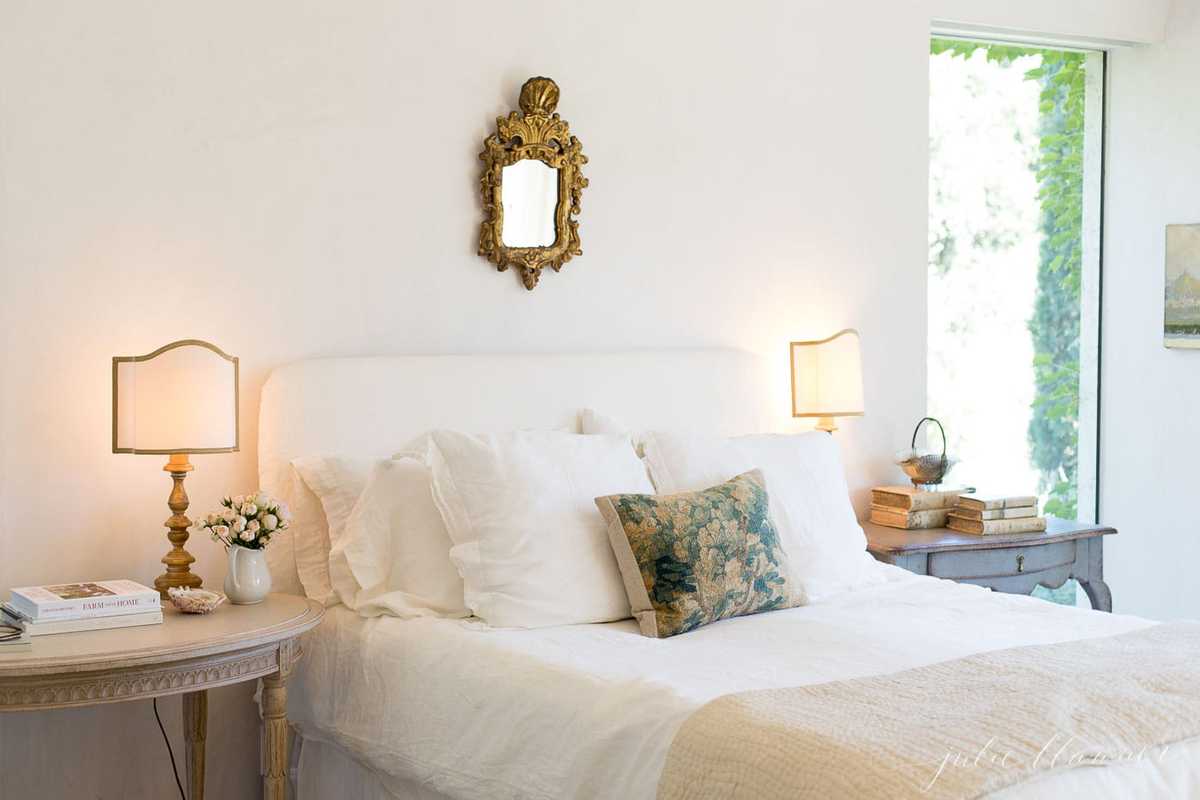 A vintage inspired bedroom with white walls, white bedding and white curtains