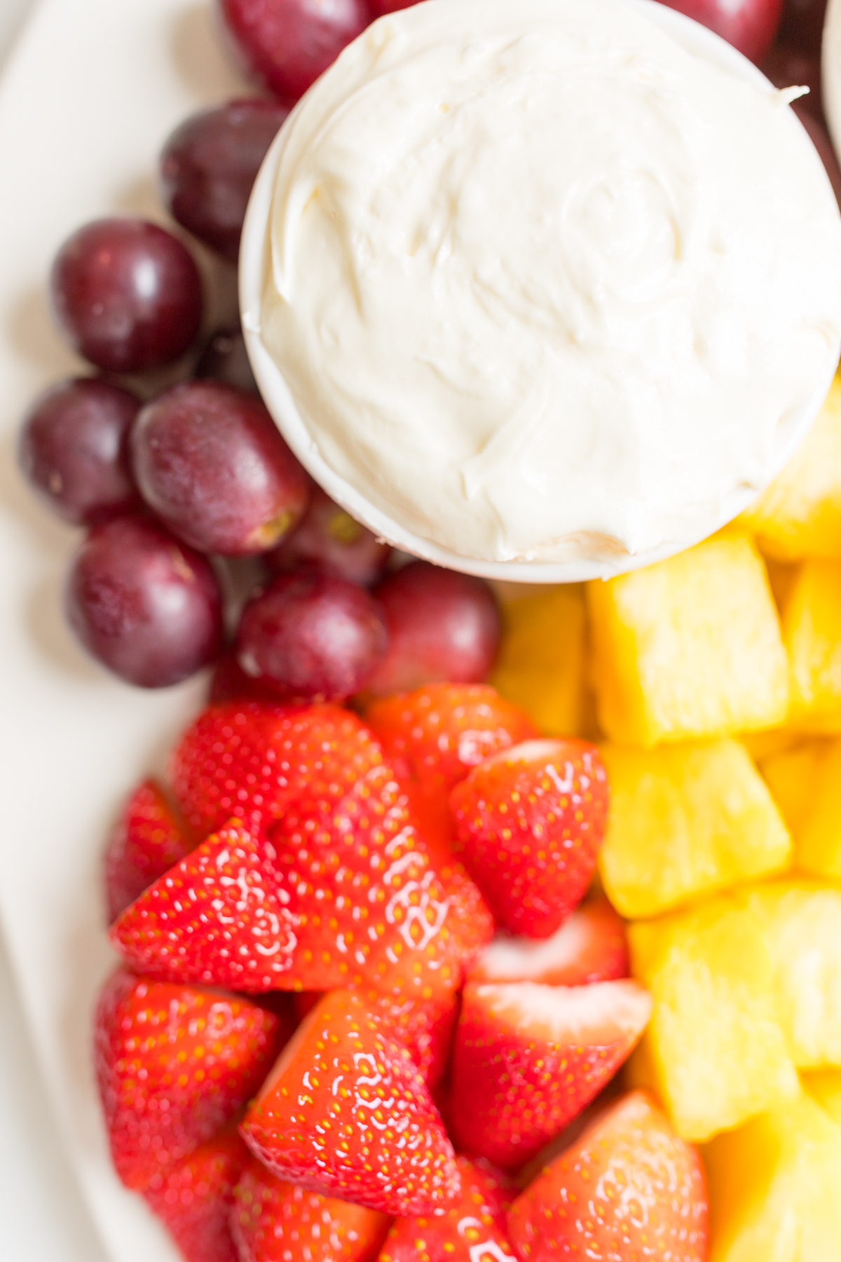 A white ceramic tray full of cut fruit and a small white bowl of cream cheese marshmallow fruit dip.