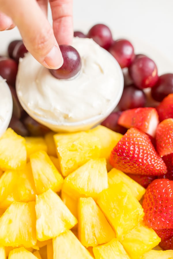 A white ceramic tray full of cut fruit and a small white bowl of cream cheese marshmallow fruit dip.