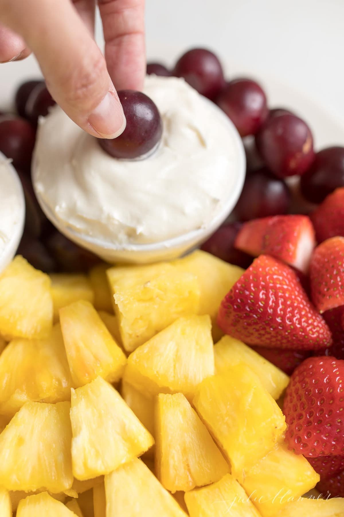 A hand dipping into a bowl full of cream cheese fruit dip