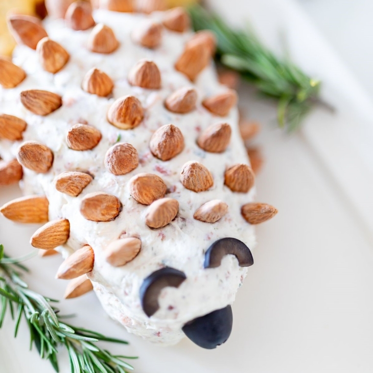 A hedgehog cheese ball on a white plate, garnished with fresh rosemary.