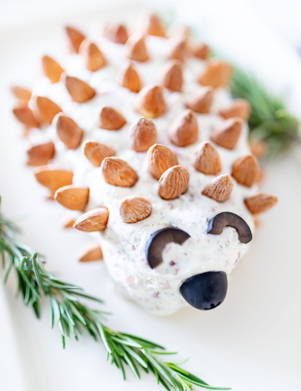 A hedgehog cheese ball on a white plate, garnished with fresh rosemary.